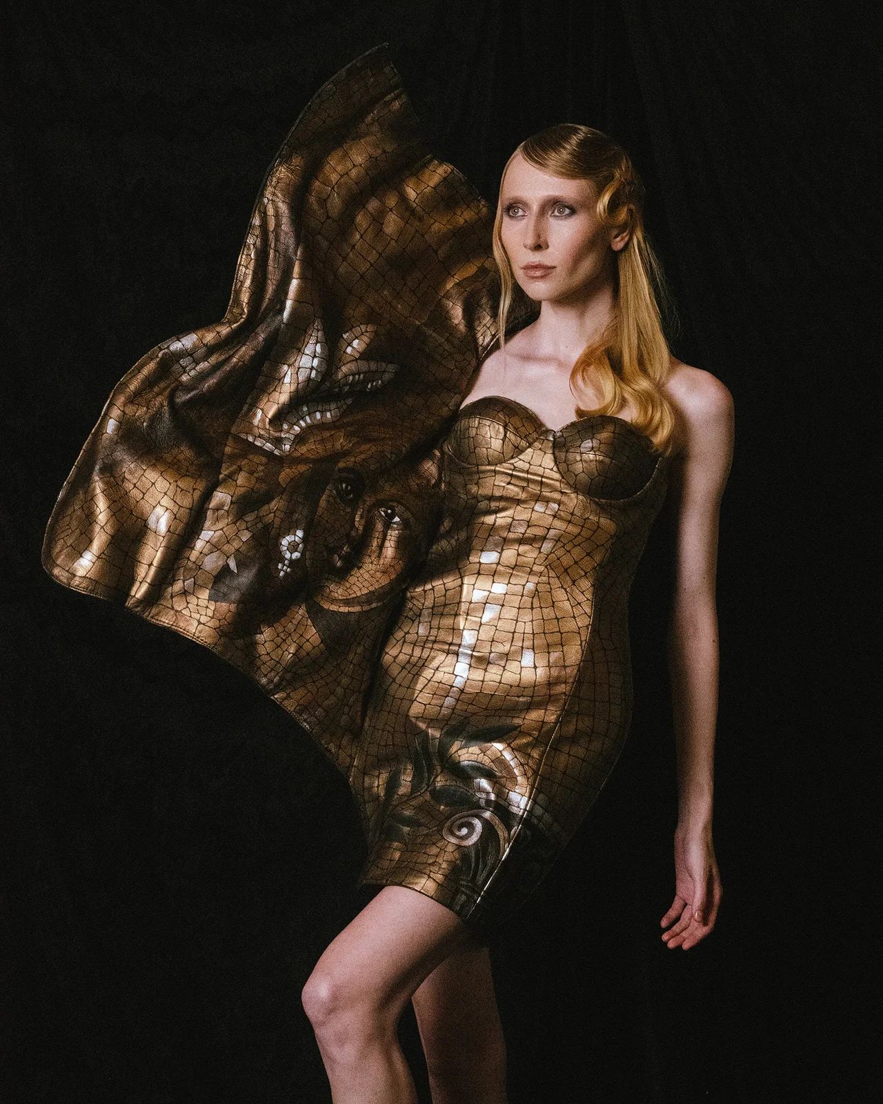 Alina in un abito oro metallizzato PORPHYROZEI con motivo materico e un grande elemento scultoreo
